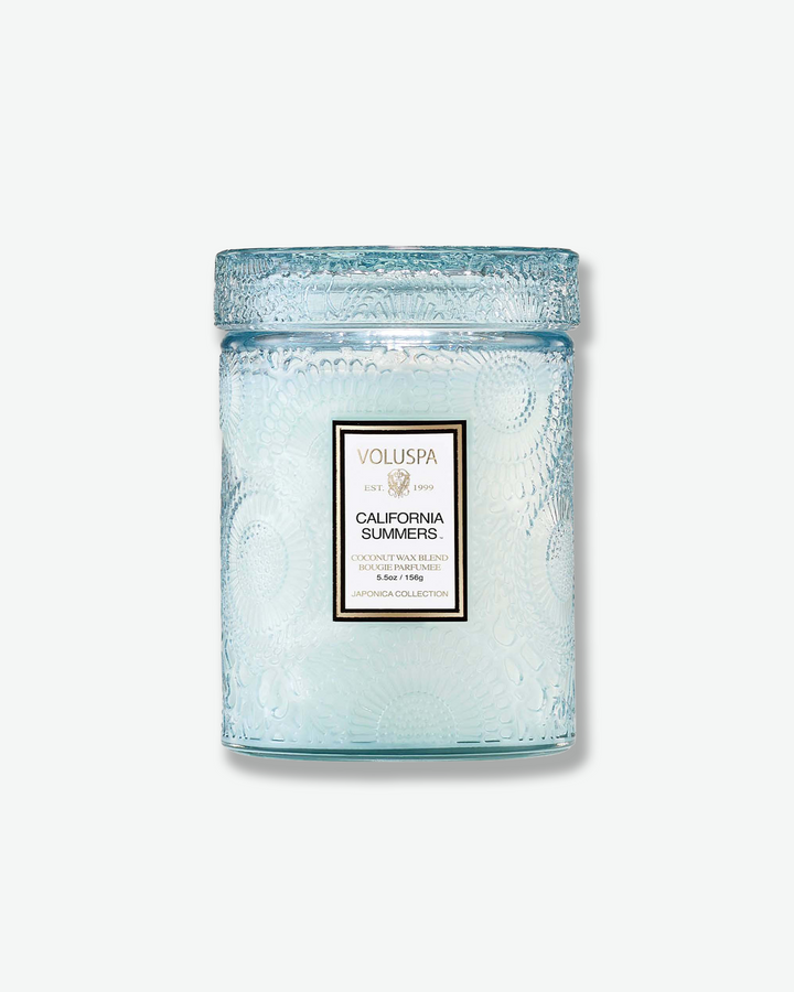Front view of a Voluspa California Summers small jar candle against a plain gray background. The translucent, light icy-blue glass vessel is completely detailed with an embossed floral pattern and capped with a matching textured glass screw-on lid.