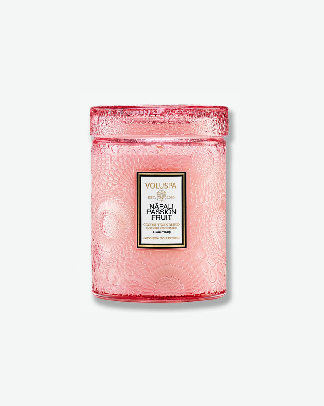 Front view of a Voluspa Nāpali Passion Fruit small jar candle against a plain gray background. The candle is enclosed in a soft pink translucent glass container beautifully embossed with floral motifs, detailed with a central rectangular label and topped with a matching textured glass screw-on lid.