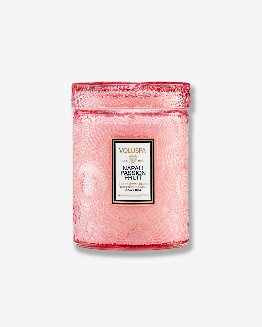 Front view of a Voluspa Nāpali Passion Fruit small jar candle against a plain gray background. The candle is enclosed in a soft pink translucent glass container beautifully embossed with floral motifs, detailed with a central rectangular label and topped with a matching textured glass screw-on lid.