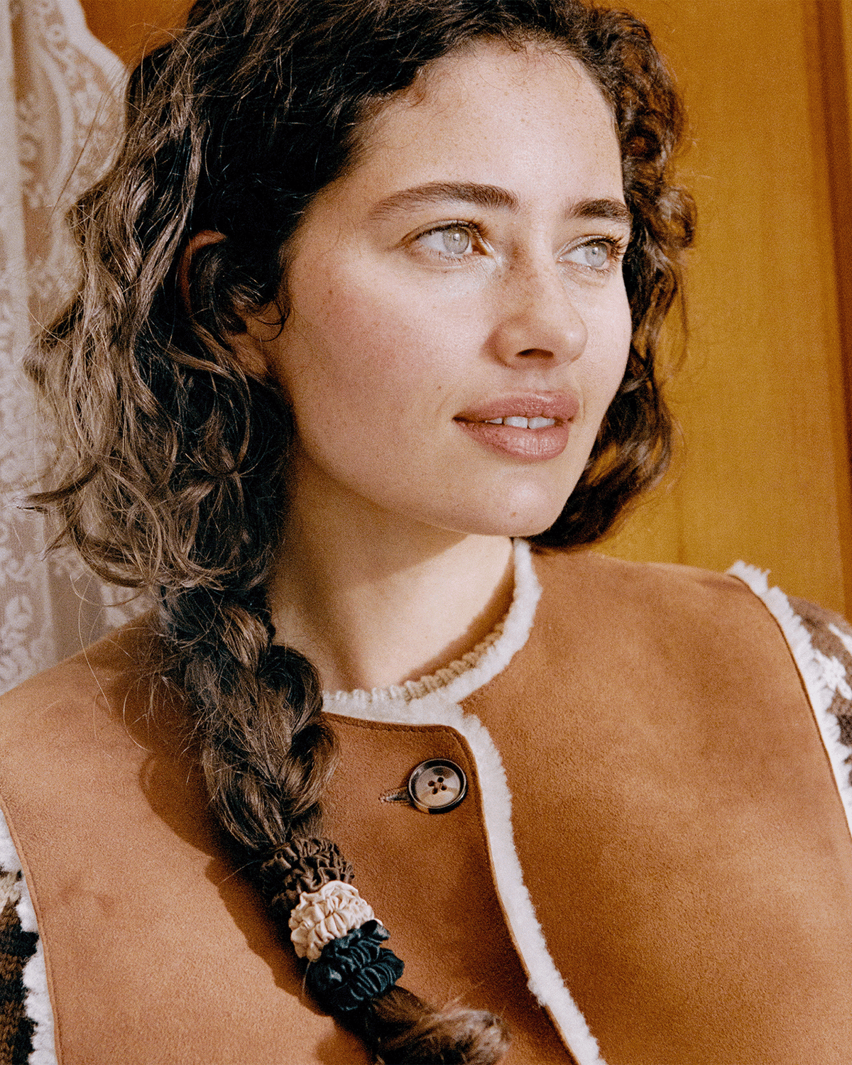 Close-up of a woman with curly brown hair styled in a loose side braid secured with Slip silk skinny scrunchies in brown, champagne, and black.