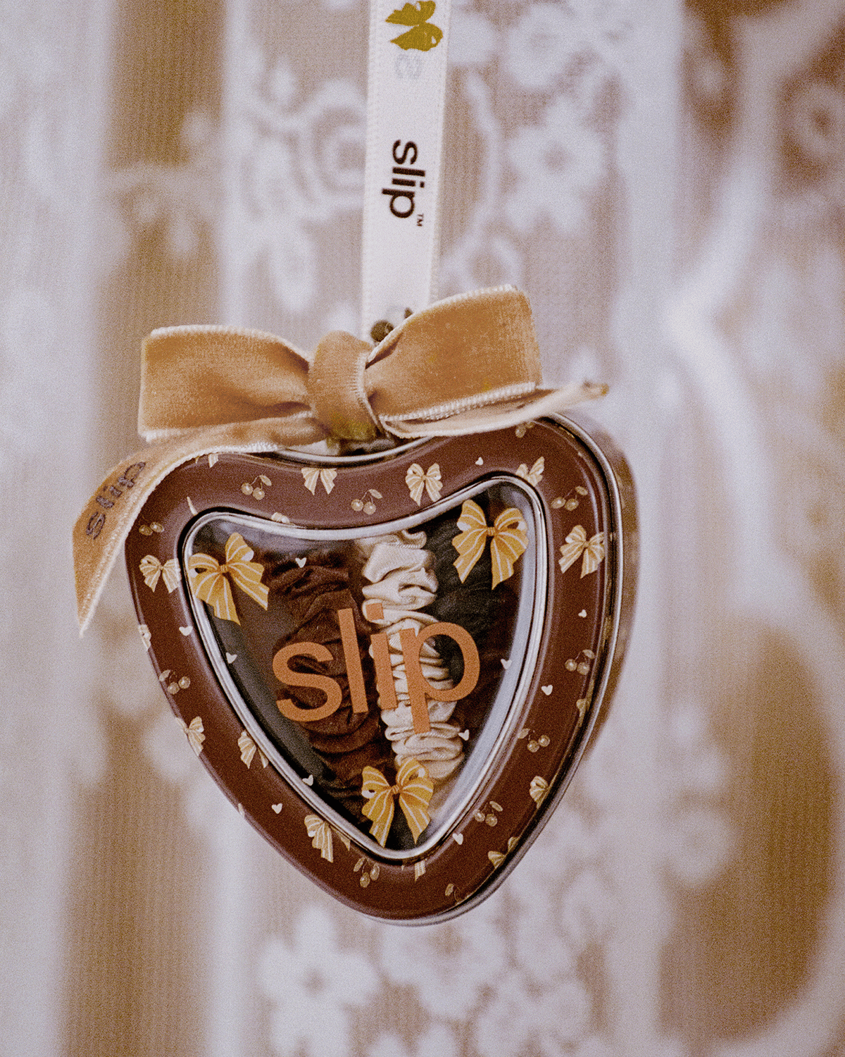 Slip holiday heart-shaped ornament featuring chocolate brown and champagne silk skinny scrunchies, decorated with gold bows and a velvet ribbon against a softly patterned background.