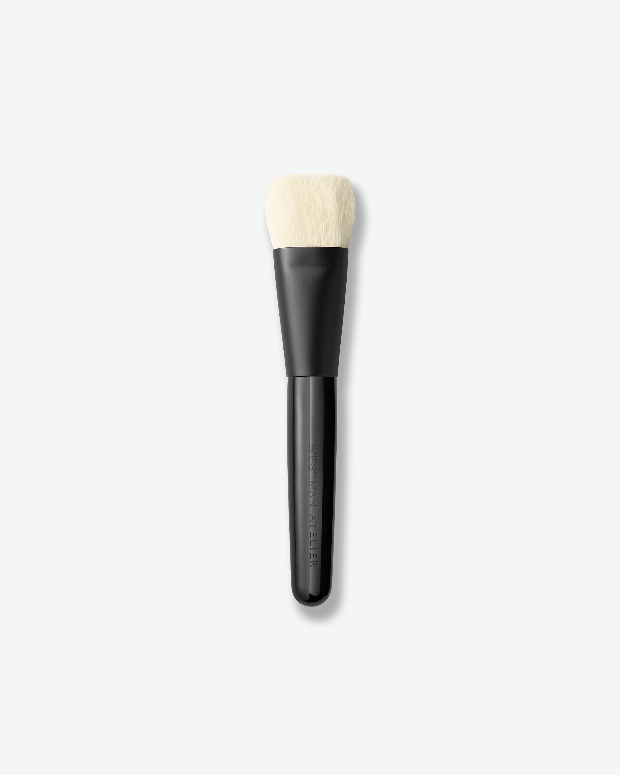 A makeup brush with a matte black handle and off-white bristles, shown vertically against a light gray background.
