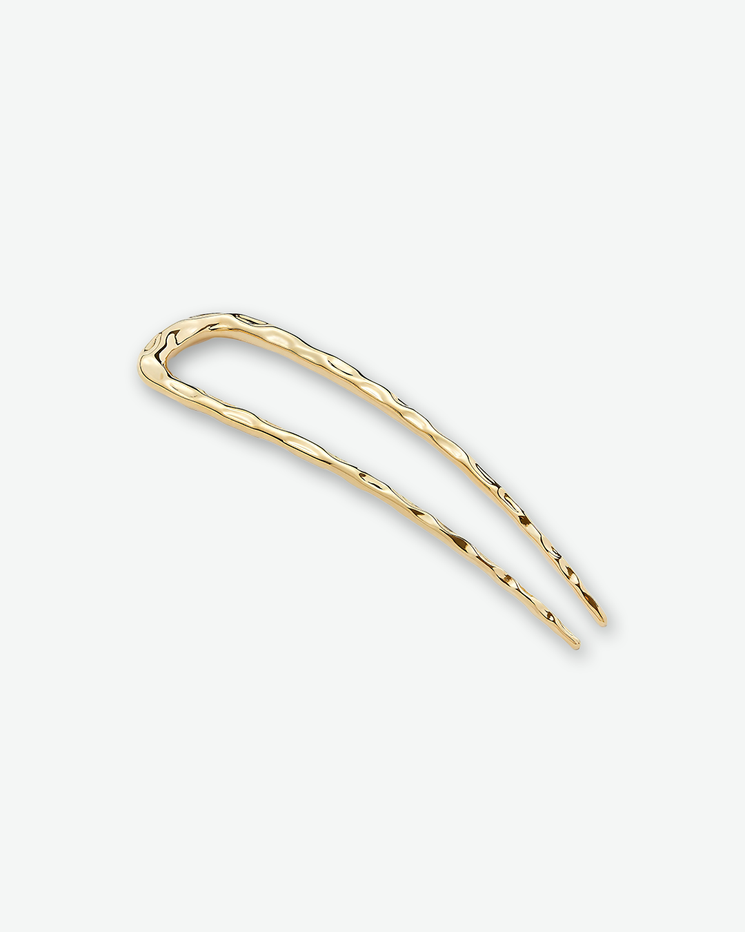A textured, u-shaped gold hair pin angled diagonally on a plain light gray background.