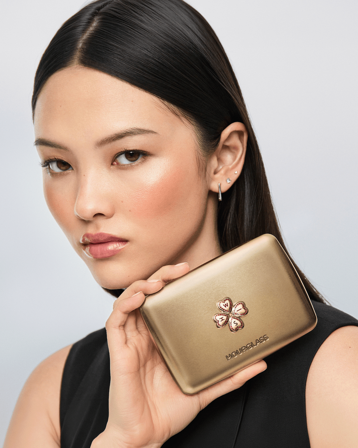 Model holding the closed gold Hourglass Wish Palette, featuring the jeweled Wish clover emblem.
