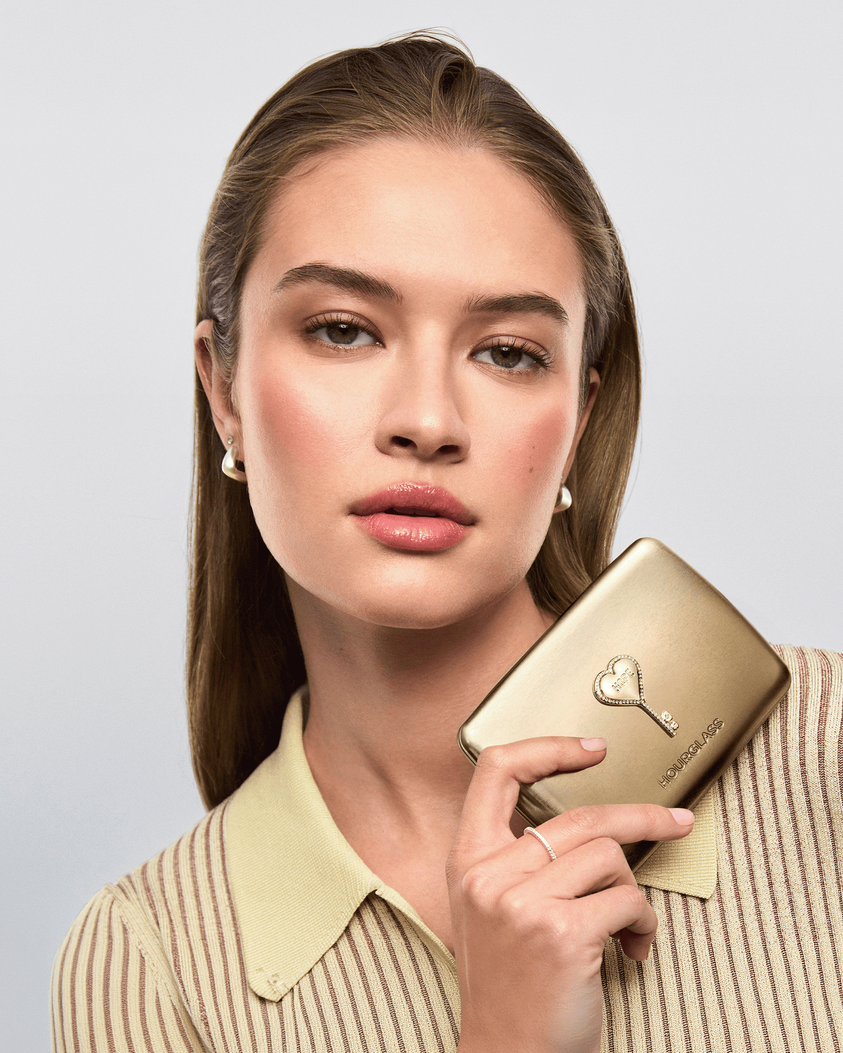 Model holding the closed gold Hourglass Ambient Lighting Edit – Unlocked Palette in Hope, featuring the decorative Hope key emblem.