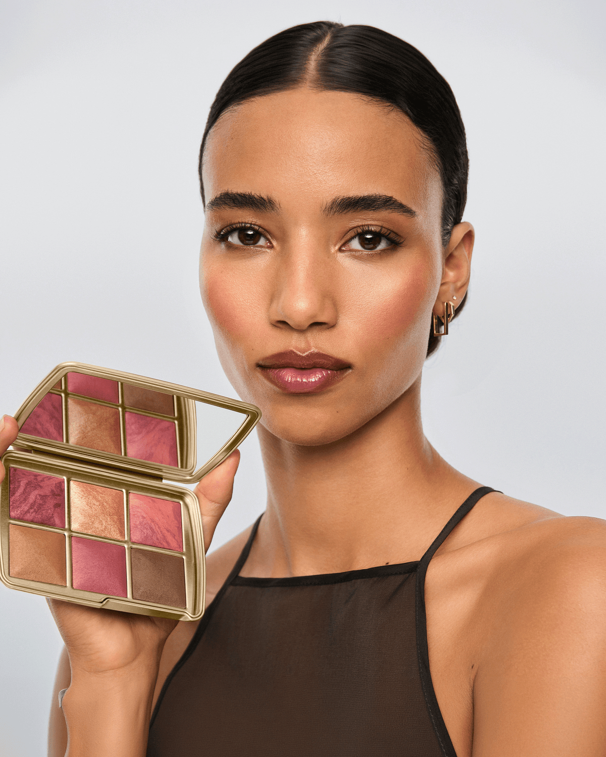 Model holding the open Hourglass Luck Palette, showcasing the six warm pink, bronze, and luminous complexion shades.