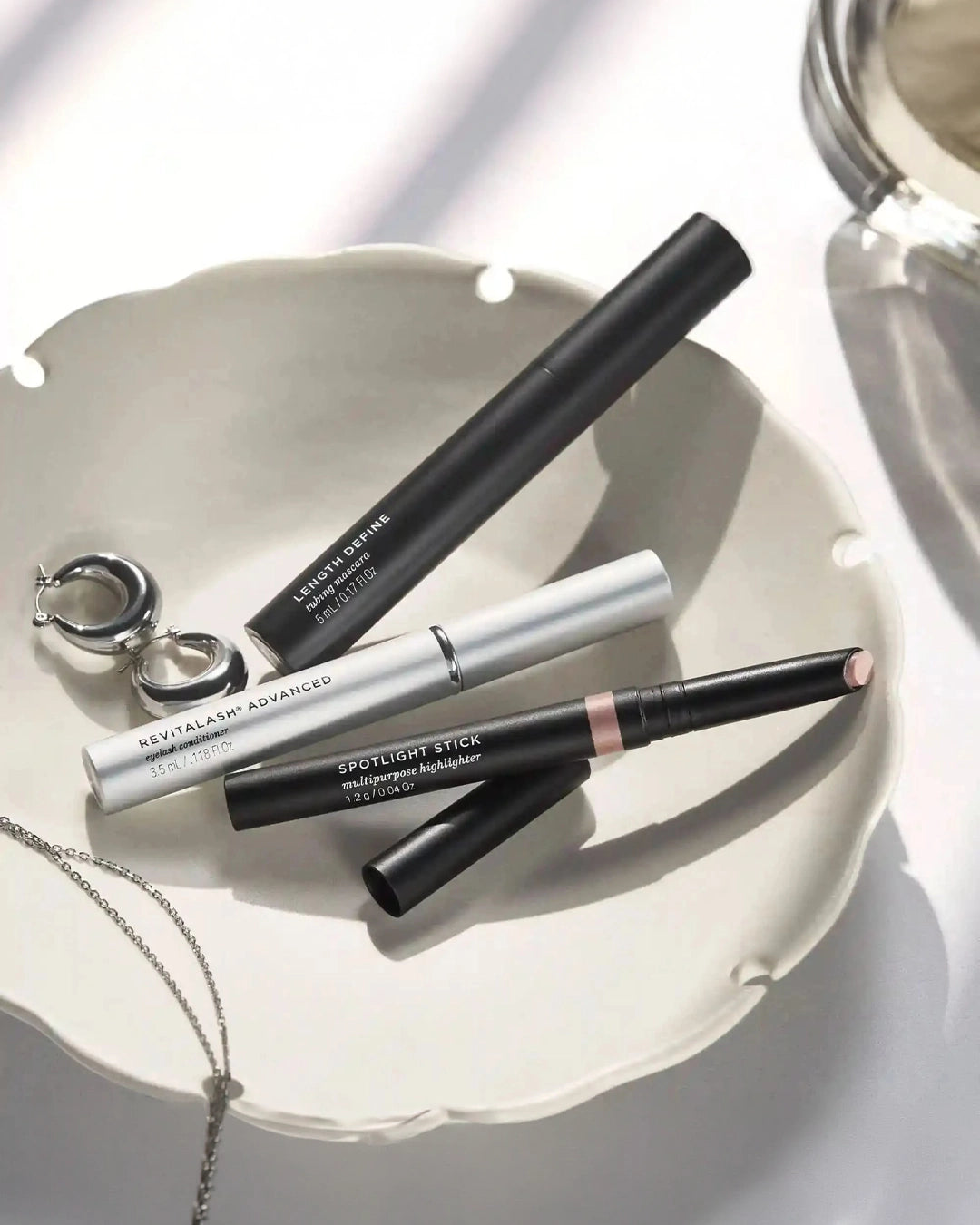 Makeup products including a eyeliner pencil, a highlighter stick, and a lip product on a white surface.
