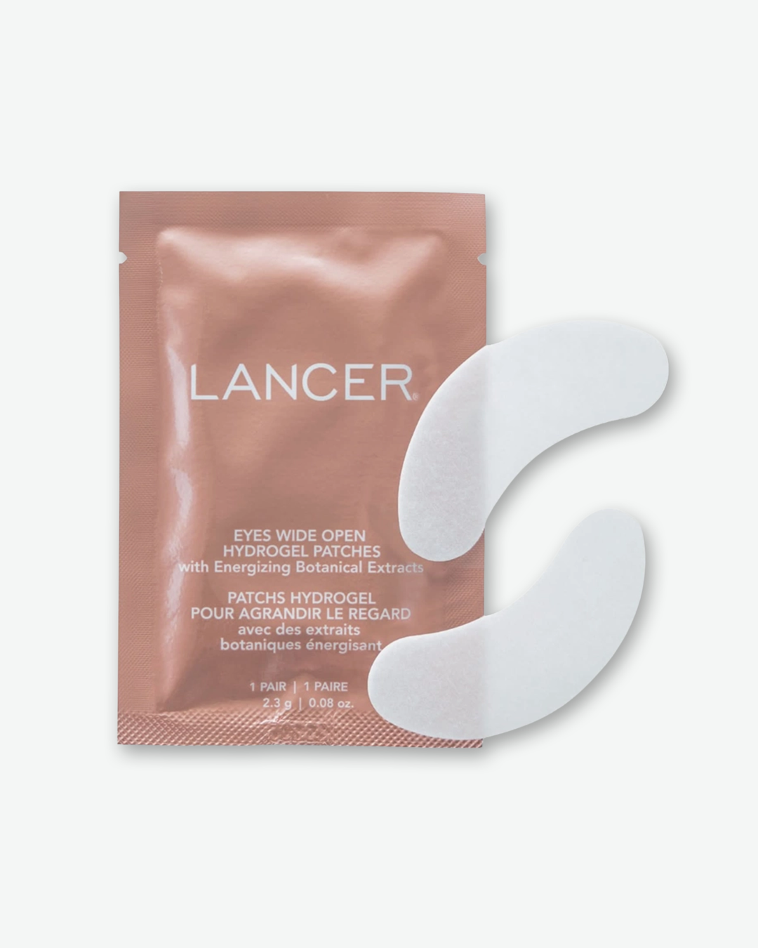 A product shot of an individual Lancer Eyes Wide Open Hydrogel Patches sachet packet alongside two eye patches, centered against a plain light gray background. The rectangular foil packet shares the same copper-bronze color and white typography as the outer box. Overlapping its right edge are two crescent-shaped, white hydrogel under-eye patches arranged in a vertical stack.