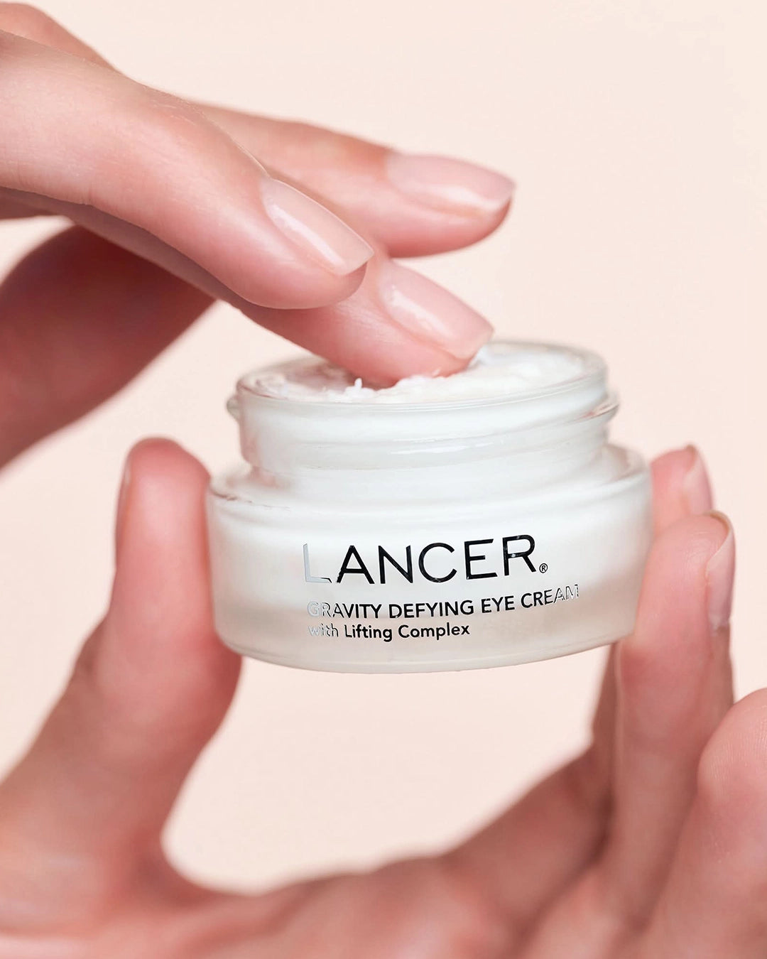 Lancer Gravity Defying Eye Cream jar held by a hand with a soft pink background