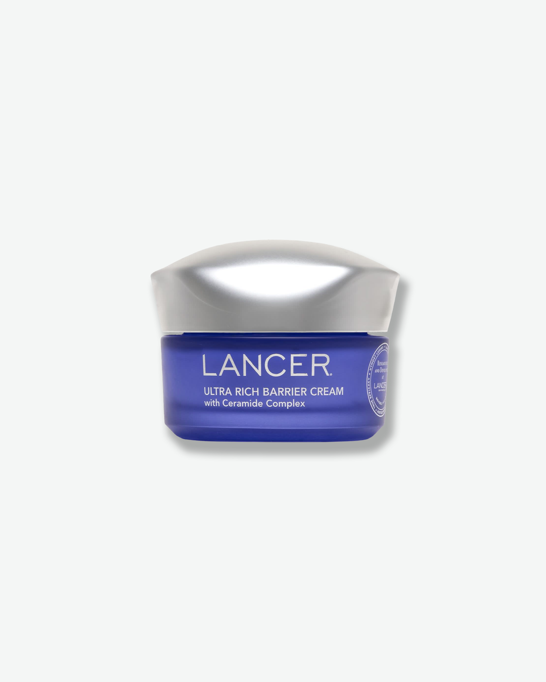 Front view of a Lancer Ultra Rich Barrier Cream jar against a plain gray background. The cosmetic container features a rich, translucent cobalt-blue glass base printed with white text, topped with a wavy, chrome metallic cap.