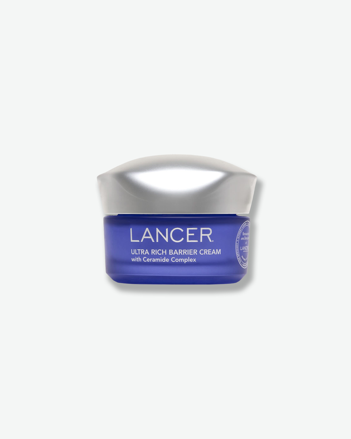 Front view of a Lancer Ultra Rich Barrier Cream jar against a plain gray background. The cosmetic container features a rich, translucent cobalt-blue glass base printed with white text, topped with a wavy, chrome metallic cap.
