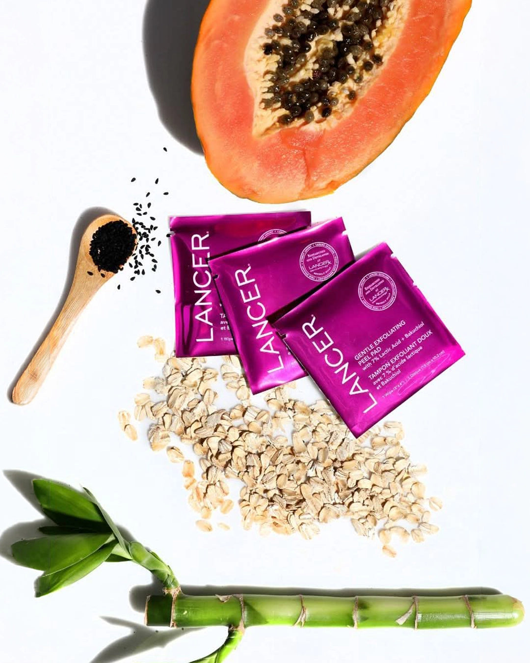 Lancer skincare packets with a papaya, wooden spoon, and bamboo shoot on a white background