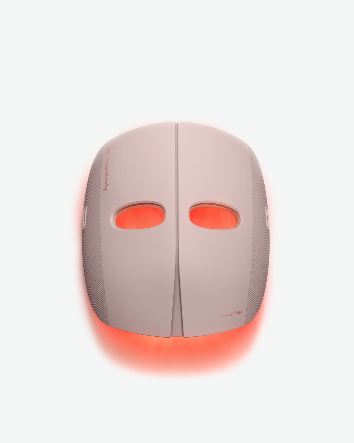Therabody TheraFace Mask in soft pink with red LED light glowing through the eye openings and around the edges.