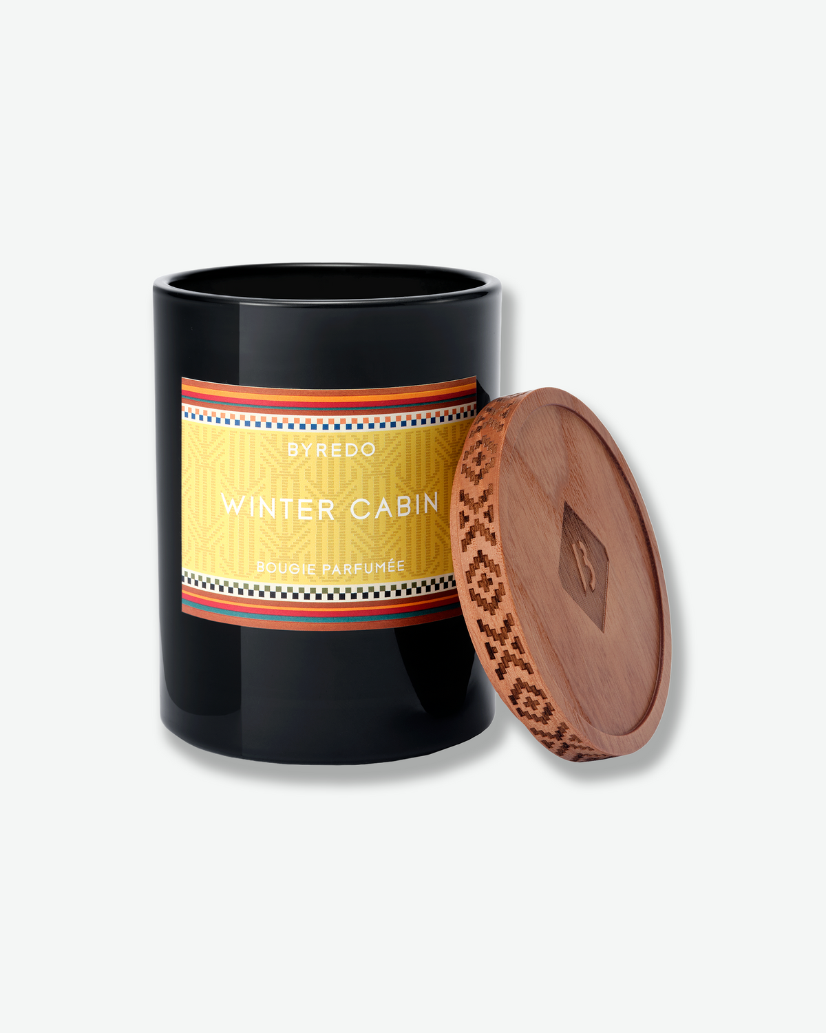 Open Byredo Winter Cabin candle with its patterned wooden lid resting beside the black glass vessel.