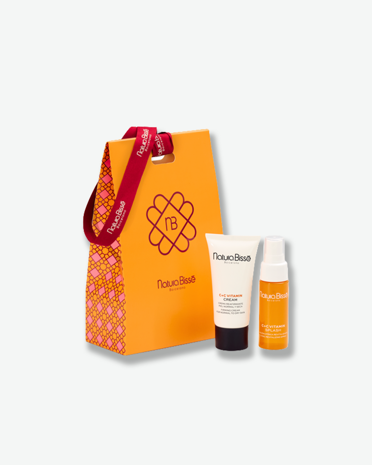 Natura Bissé C+C Vitamin skincare gift set featuring C+C Vitamin Cream and C+C Vitamin Splash, displayed alongside a vibrant orange gift bag with a red branded ribbon.