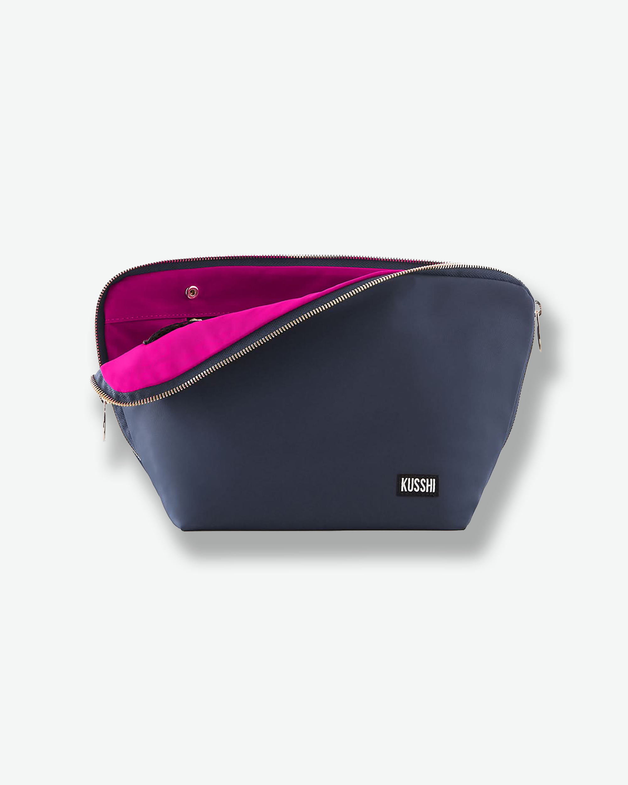 Front view of a large navy blue fabric KUSSHI makeup bag. The main gold zipper is partially open, pulling back to showcase a vibrant hot pink fabric interior lining, accented by a black and white brand label on the bottom right.