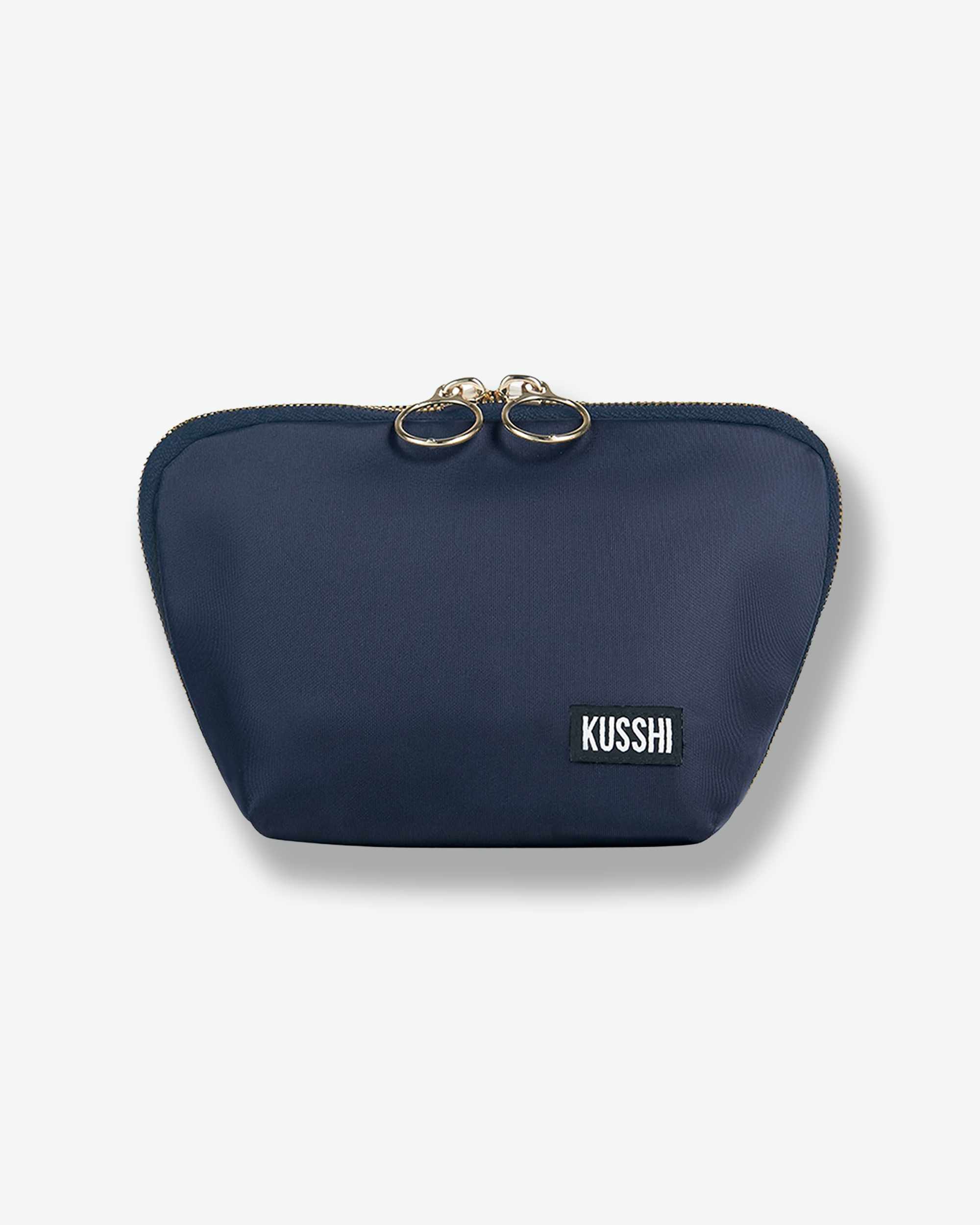 Front view of the medium navy blue fabric KUSSHI makeup bag shown completely closed, highlighting the clean fabric structure and dual gold circular ring zipper pulls.