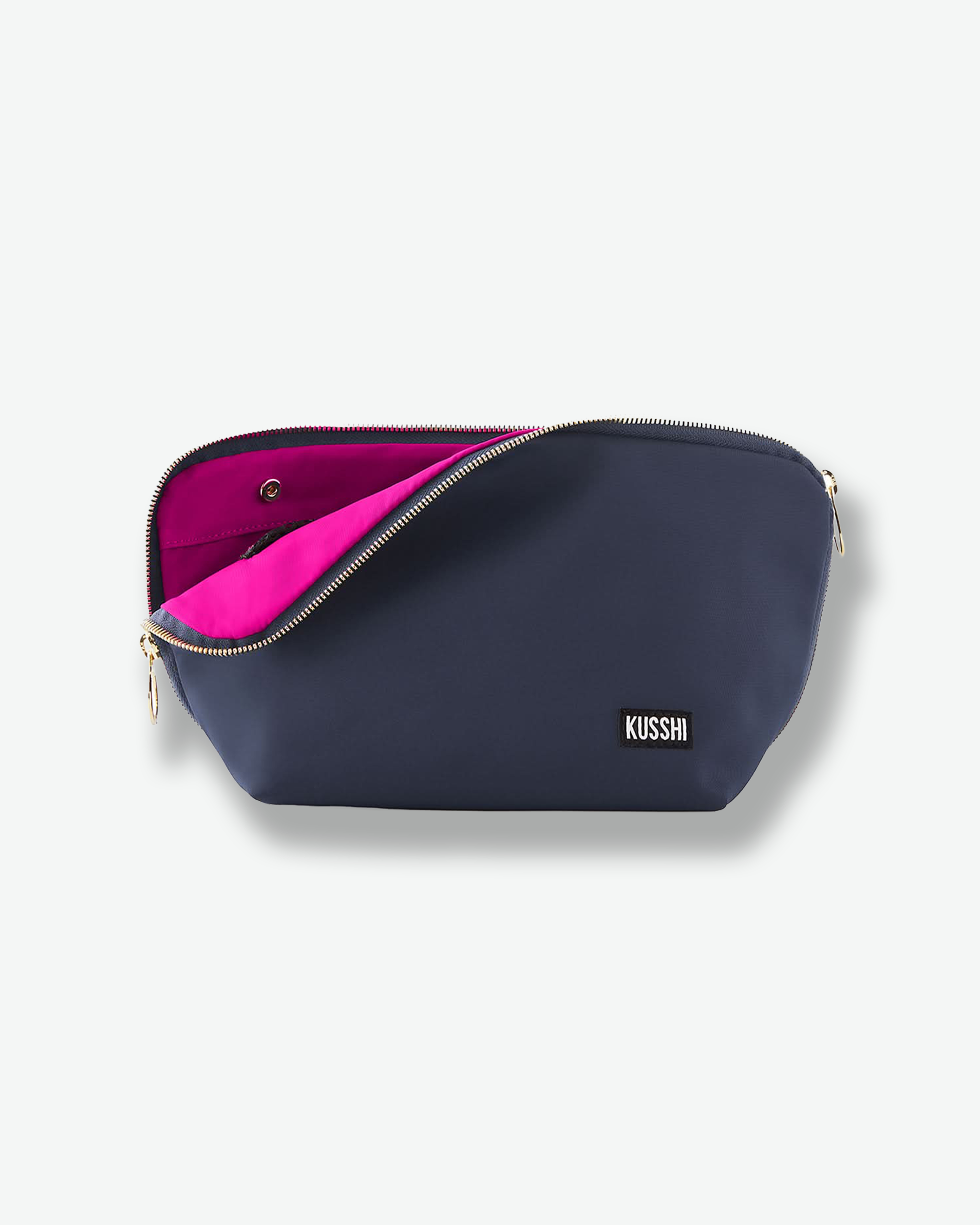 Front view of a small navy blue fabric KUSSHI makeup bag. The top gold zipper is unzipped halfway to flash the vivid hot pink interior, with the square black-and-white logo badge positioned on the lower right.