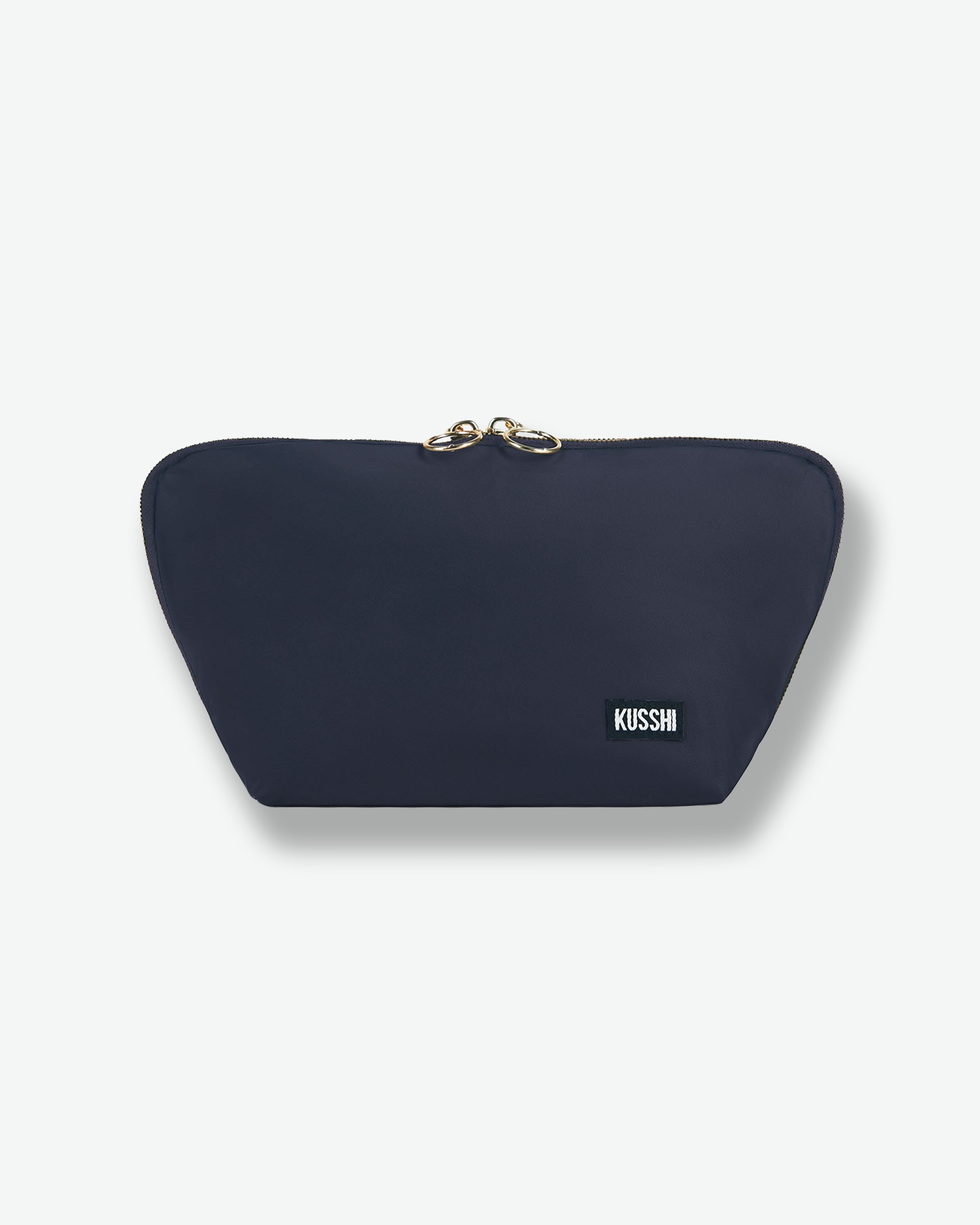Front view of the small navy blue fabric KUSSHI makeup bag zipped completely closed, showing its compact design and decorative gold ring zipper pulls.