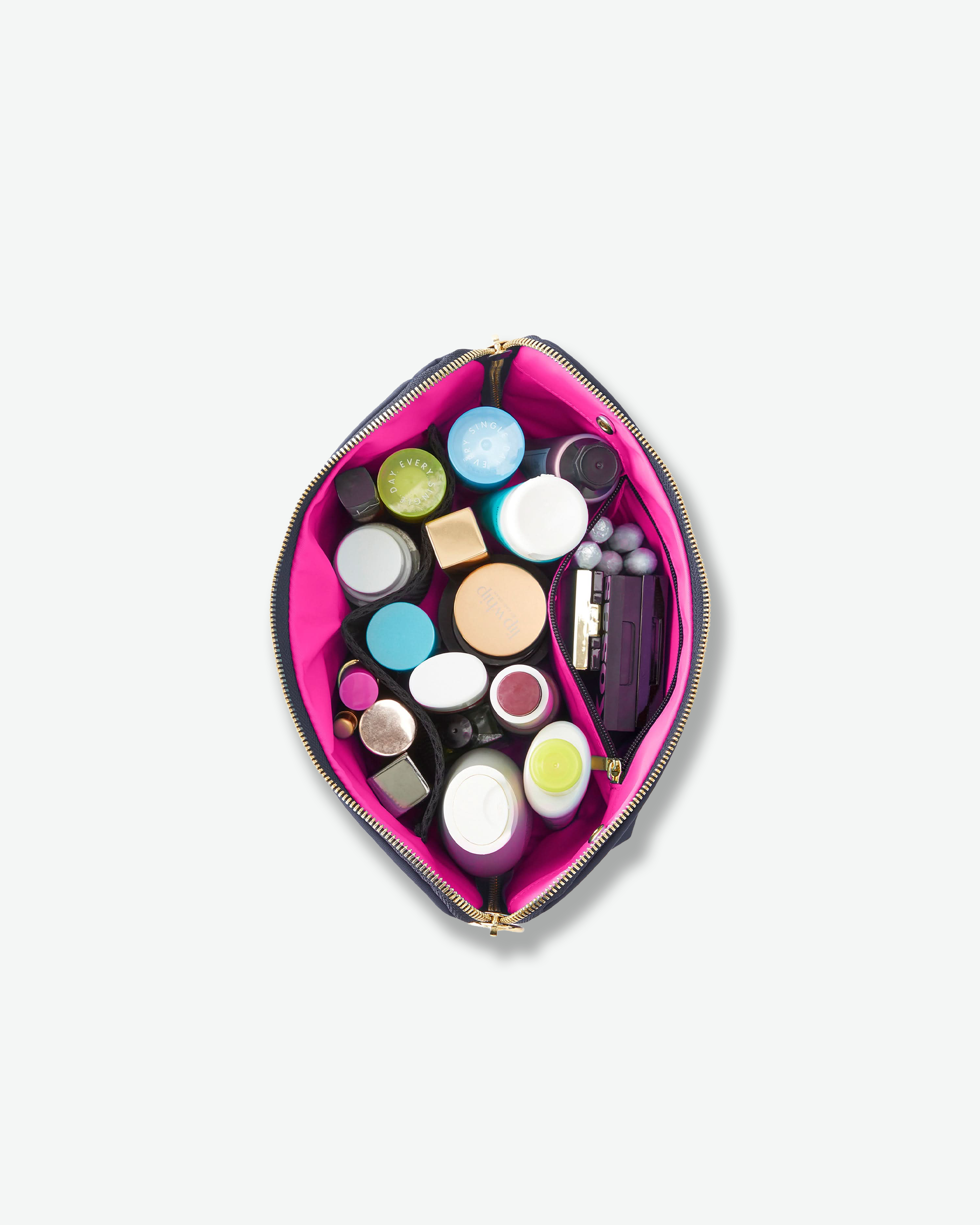 A bright pink zippered cosmetic pouch shown open from above, filled with assorted makeup items and containers on a plain light gray background.