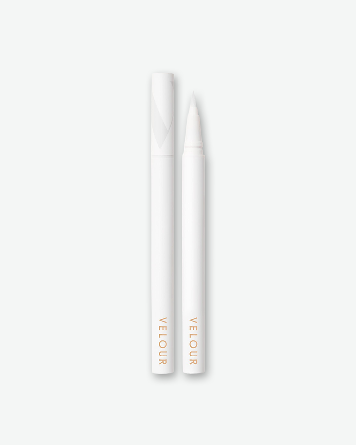 Product shot of a Velour liquid eyeliner pen shown next to its detached cap against a plain gray background. Both the slender pen and cap feature a matte white finish with minimalist gold branding text at the base. The pen is uncapped to display its fine, tapered precision felt tip.