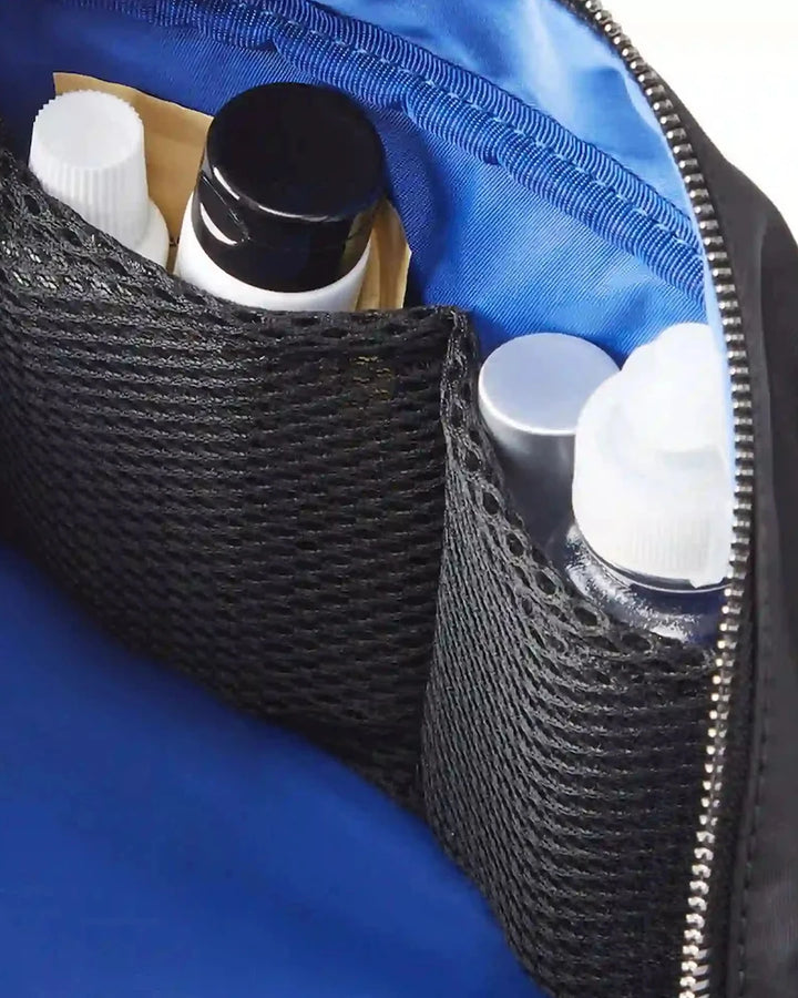 Blue toiletry bag with black mesh pocket containing skincare products.