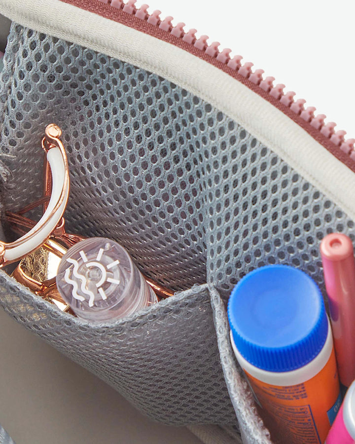Close-up of a pouch with a eyelash curler, bottle, and makeup inside.