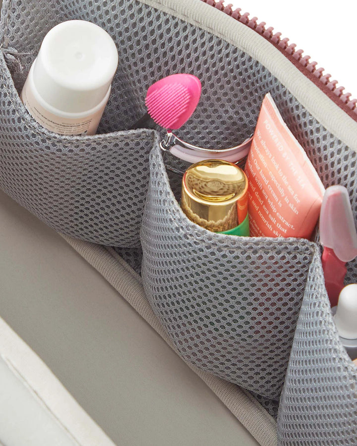 Gray mesh pouch with cosmetic items including a gold bottle and pink brush.