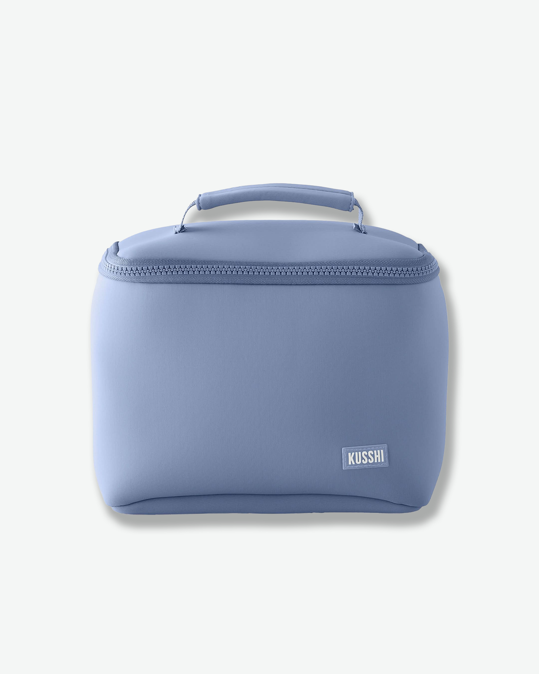 A studio product shot of a structured, periwinkle blue fabric makeup bag from Kusshi against a light gray background. The rectangular bag features rounded sides, a matching blue zipper closure that wraps around the upper edge, and a sturdy top handle. A small, rectangular white logo patch with the word 'KUSSHI' is stitched onto the bottom right corner.