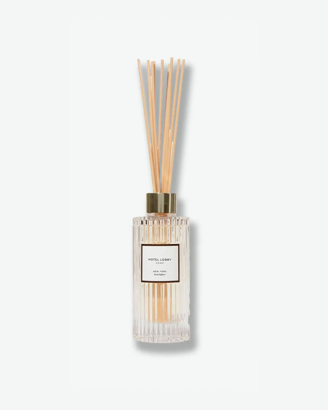 Hotel Lobby Home New York Reed Diffuser featuring a fluted clear glass bottle filled with clear liquid and light wooden reeds extending upward, isolated against a light grey background.