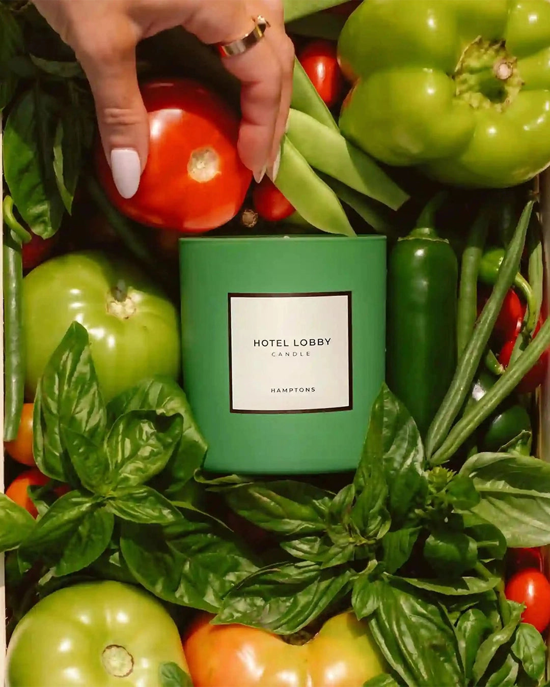 Green candle labeled 'Hotel Lobby' surrounded by fresh vegetables and herbs