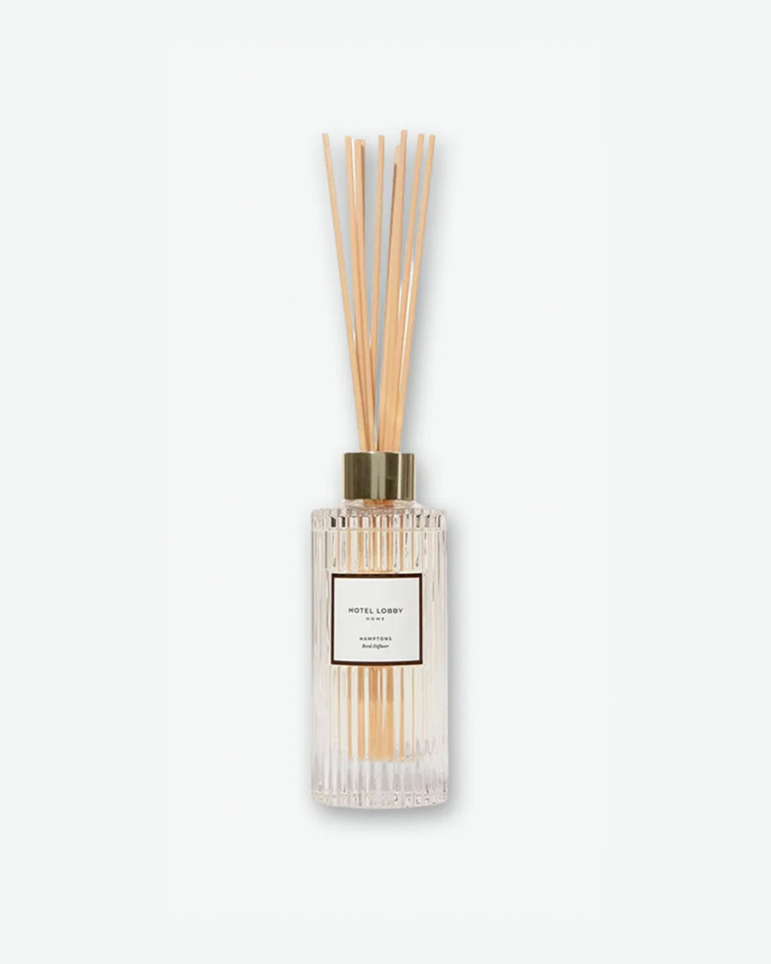 Hotel Lobby Home Hamptons Reed Diffuser featuring a fluted clear glass bottle filled with clear liquid and light wooden reeds extending upward, isolated against a light grey background.