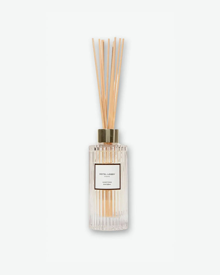 Hotel Lobby Home Hamptons Reed Diffuser featuring a fluted clear glass bottle filled with clear liquid and light wooden reeds extending upward, isolated against a light grey background.