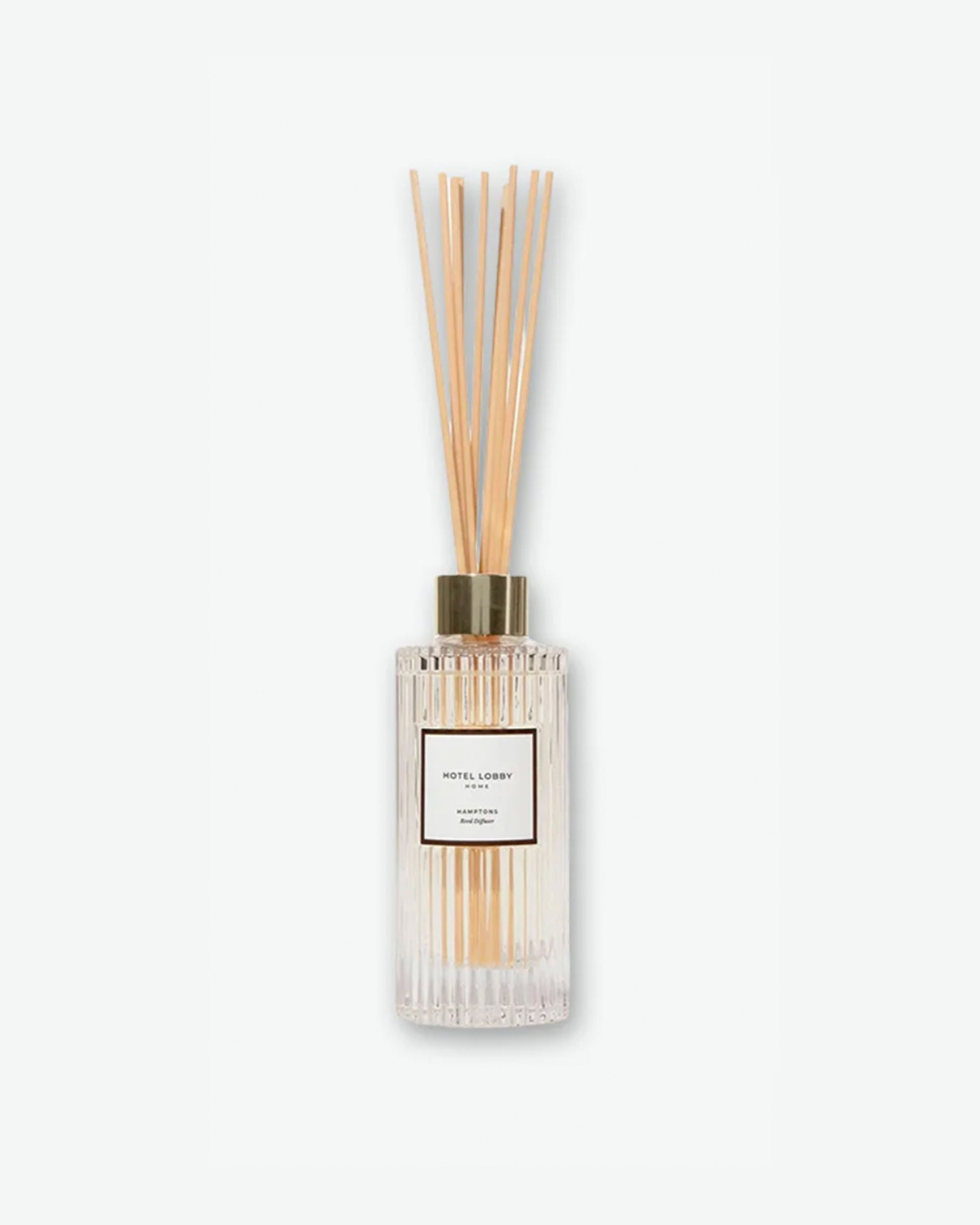 Hotel Lobby Home Hamptons Reed Diffuser featuring a fluted clear glass bottle filled with clear liquid and light wooden reeds extending upward, isolated against a light grey background.