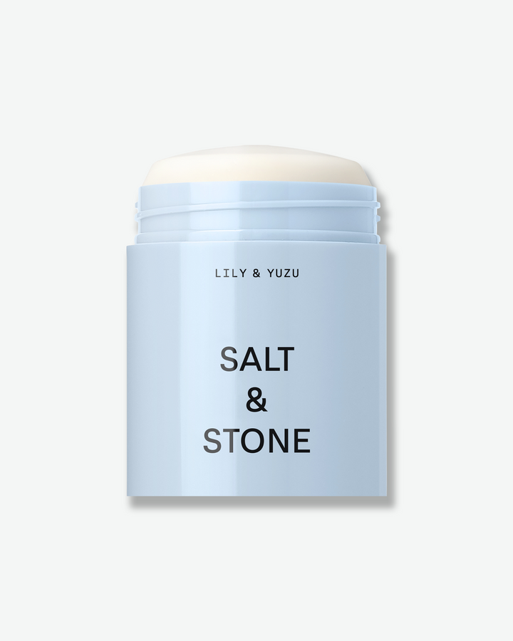 An open, light blue container of Salt & Stone "Lily & Yuzu" deodorant stick showing the product inside against a white background.