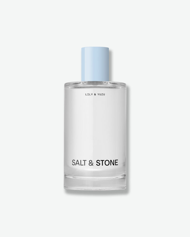 Clear glass bottle of Salt & Stone "Lily & Yuzu" fragrance with a light blue cap against a white background.