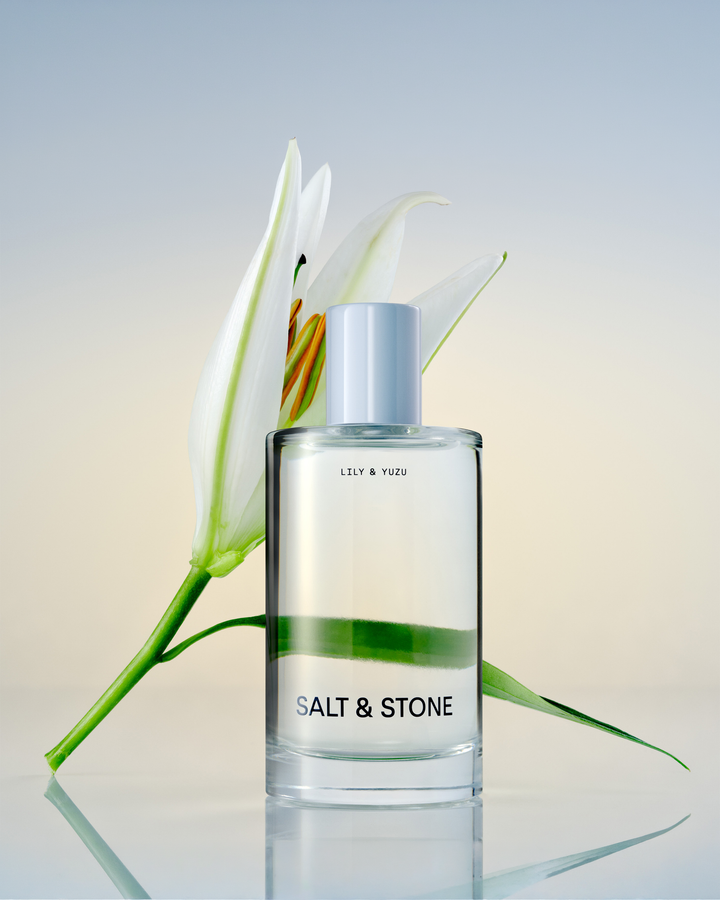 Salt & Stone Lily & Yuzu fragrance bottle next to a white lily.