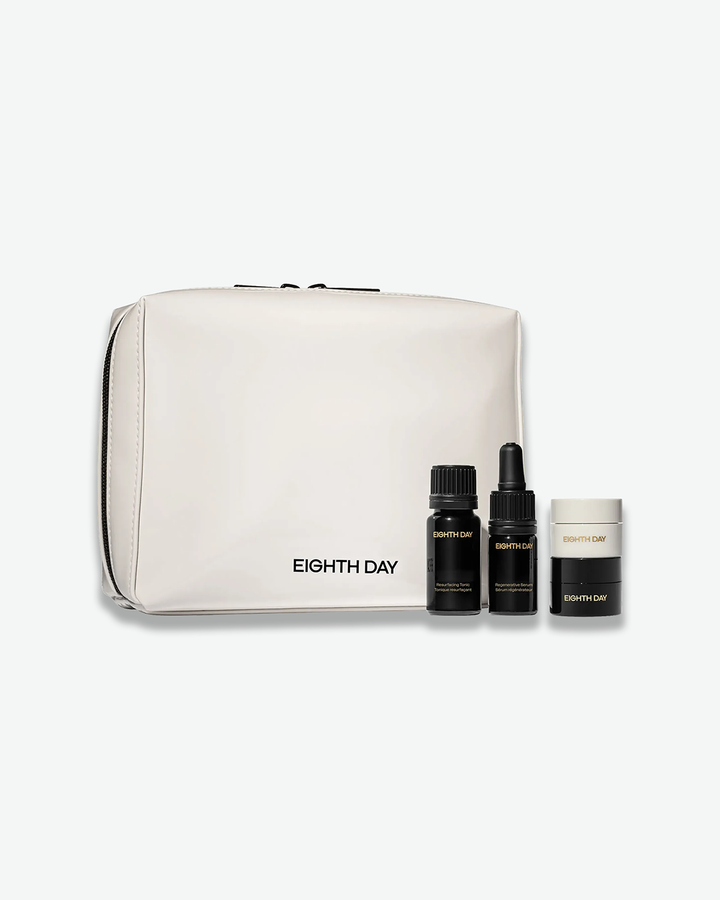 A product shot of the Eighth Day Discovery Set against a light gray background. In the background sits a structured, rectangular cream-white travel pouch with a black zipper and "EIGHTH DAY" printed in black text at the bottom. In front of the pouch stand three miniature products: a dark glass Resurfacing Tonic bottle, a dark glass Regenerative Serum dropper bottle, and a small stacked black-and-white cream jar.