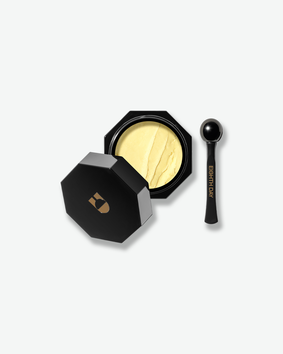 Black octagonal Eight Day eye cream jar opened to reveal pale yellow cream, with a black spherical applicator beside it on a light background.
