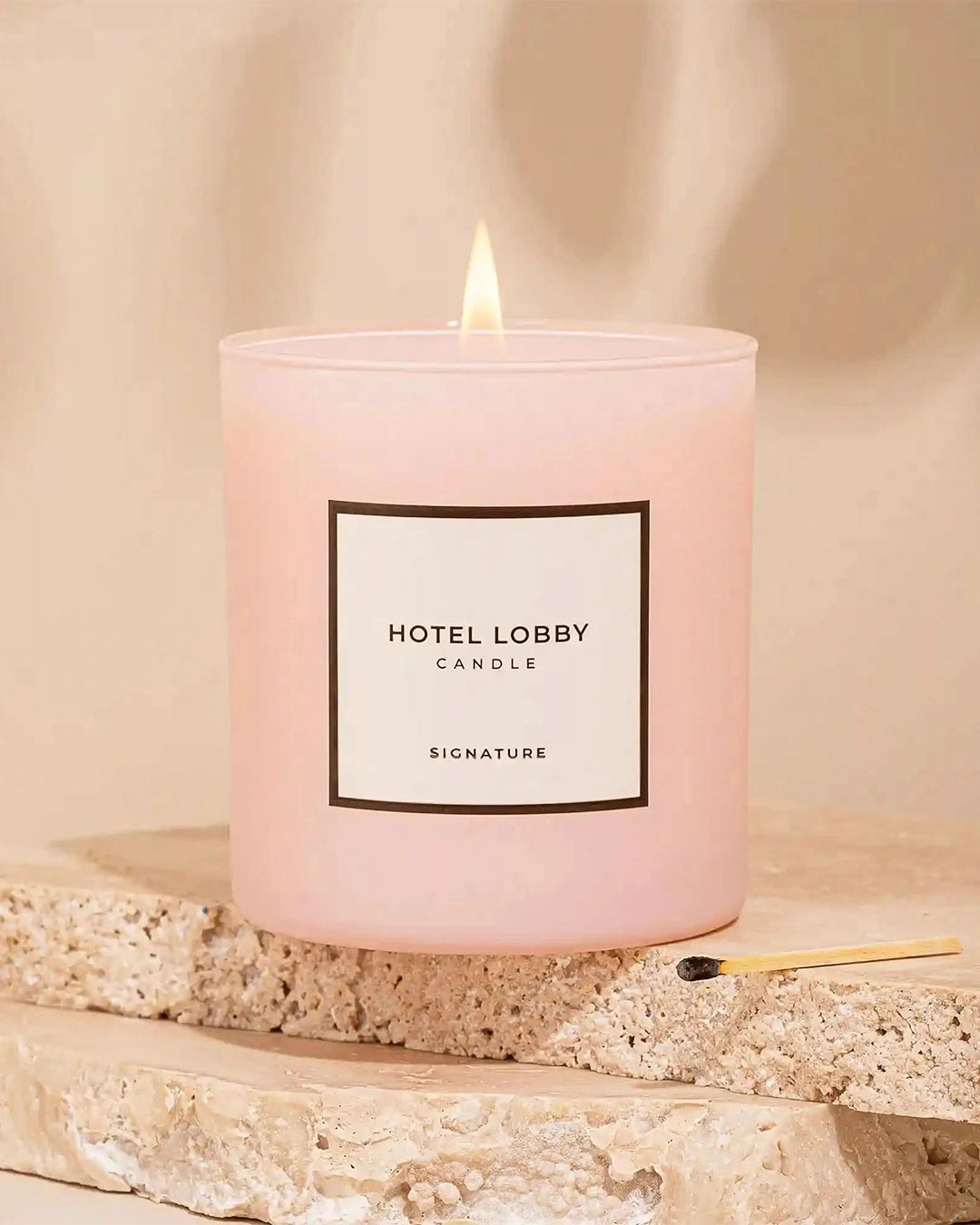 Pink candle labeled 'Hotel Lobby Candle' on a textured surface with a match next to it.