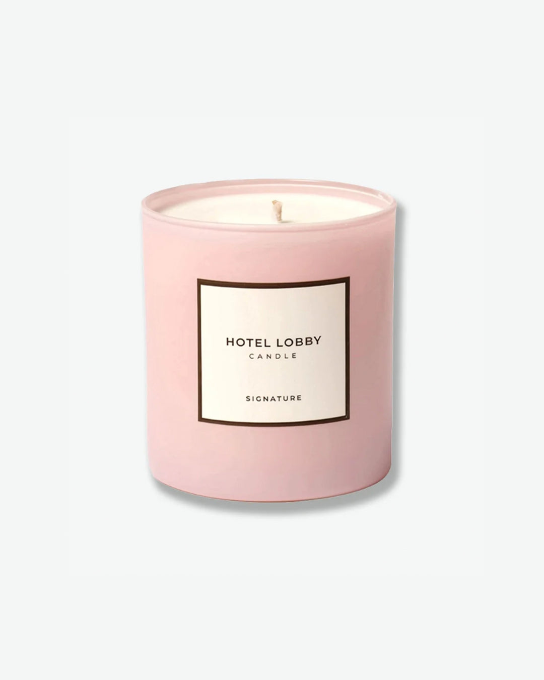 Hotel Lobby Candle Signature scented candle in a matte pastel pink glass tumbler with a square white label, isolated against a light grey background.
