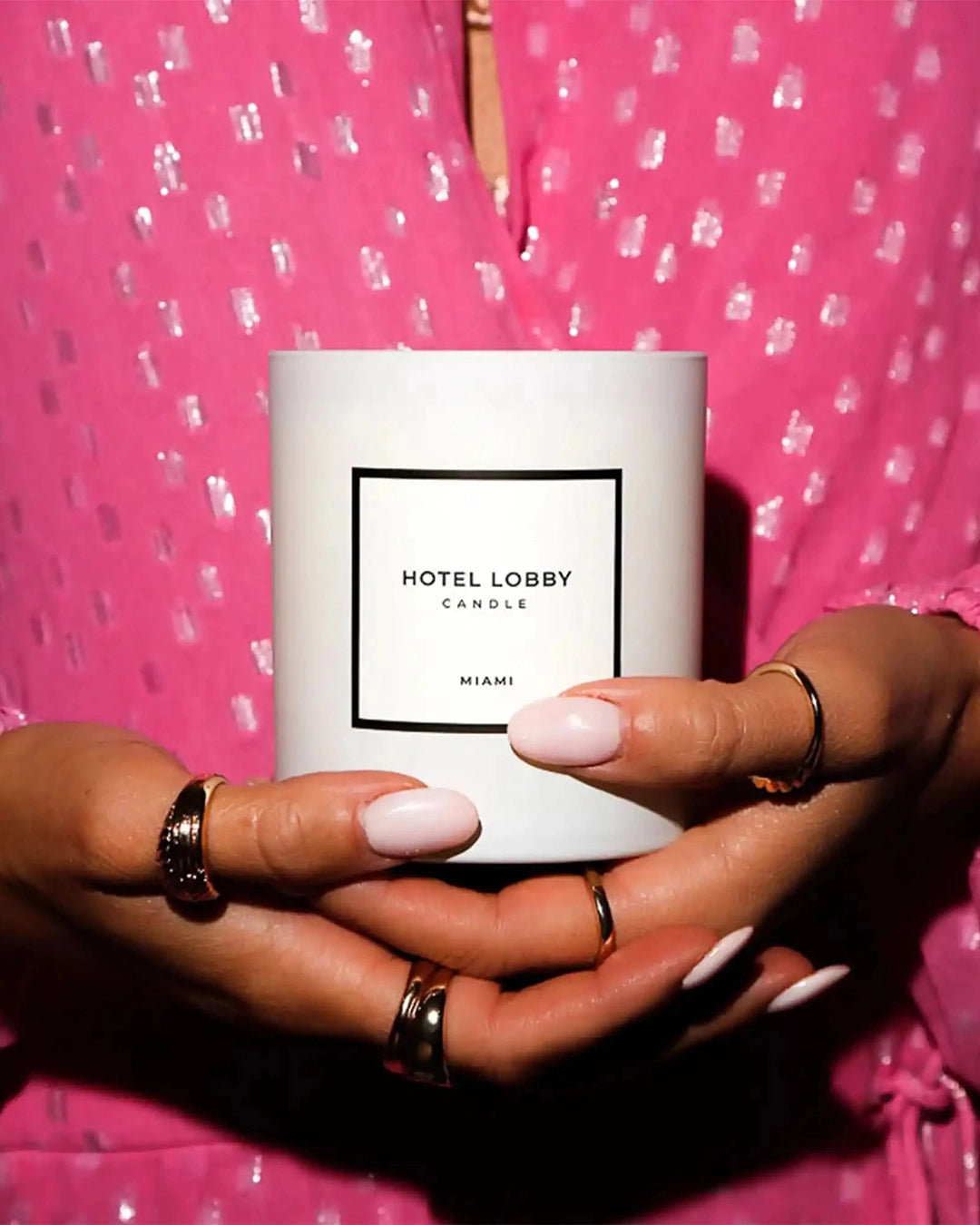 Person holding a 'Hotel Lobby' candle with a pink polka dot background