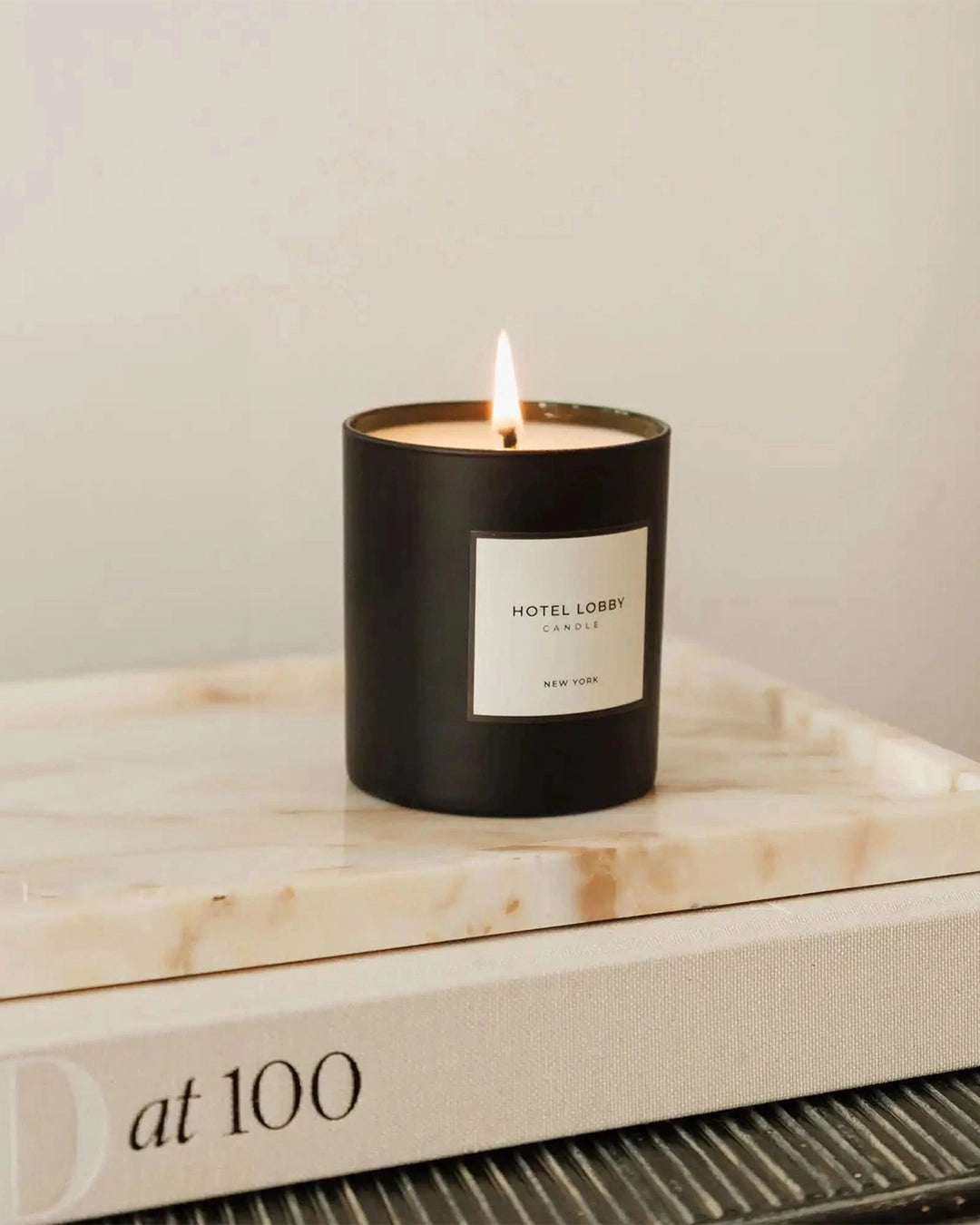 Candle in a black container labeled 'Hotel Lobby' on a marble surface with a neutral background