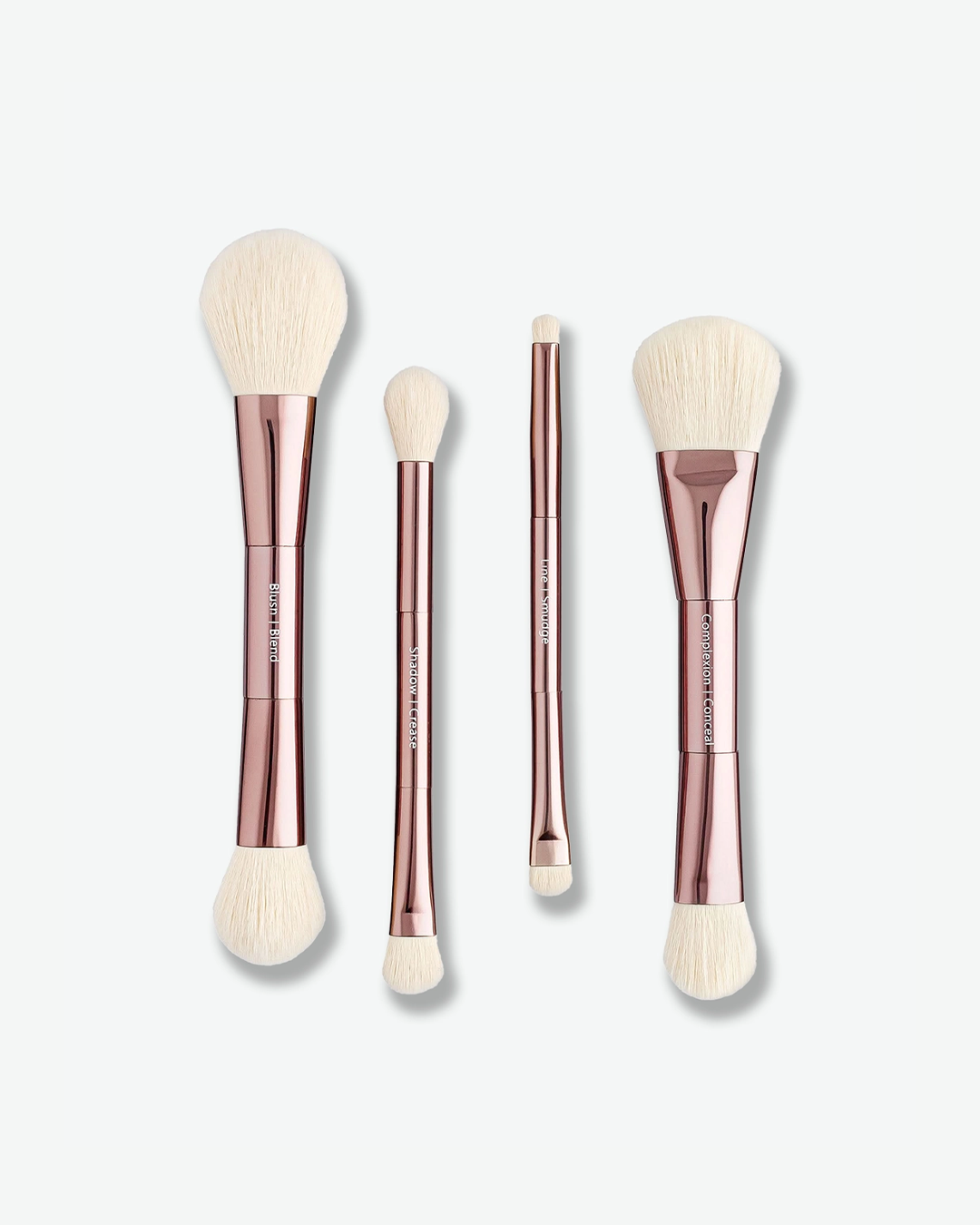 A product shot displaying four double-ended makeup brushes arranged vertically against a plain light gray background. The brushes feature shiny rose-gold handles with white text designating the brush functions—such as "Blush / Blend", "Shadow / Crease", "Line / Smudge", and "Complexion / Conceal"—and are tipped with white bristles on both ends.