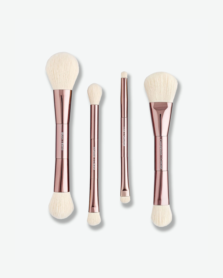 A product shot displaying four double-ended makeup brushes arranged vertically against a plain light gray background. The brushes feature shiny rose-gold handles with white text designating the brush functions—such as "Blush / Blend", "Shadow / Crease", "Line / Smudge", and "Complexion / Conceal"—and are tipped with white bristles on both ends.