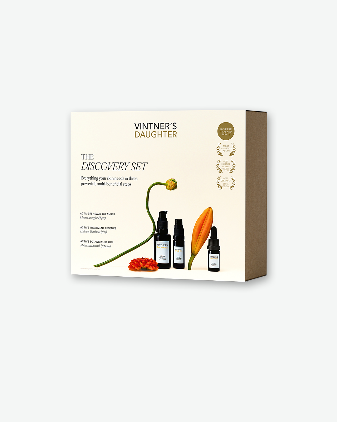 A clean, eye-level product shot of the Vintner's Daughter Discovery Set packaging. The square cream-colored box has a brown cardboard side panel and displays the text 'Vintner's Daughter The Discovery Set' with a three-step routine description. An artistic, looping green flower stem with an orange petal sits at the bottom, framed next to three miniature dark amber skincare bottles.