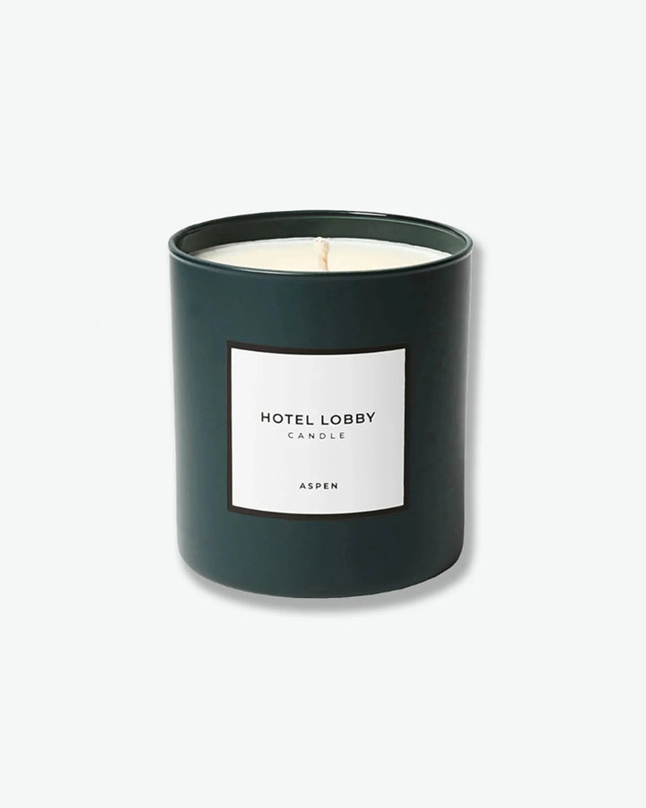Hotel Lobby Candle Aspen scented candle in a matte forest green glass tumbler with a square white label, isolated against a light grey background.