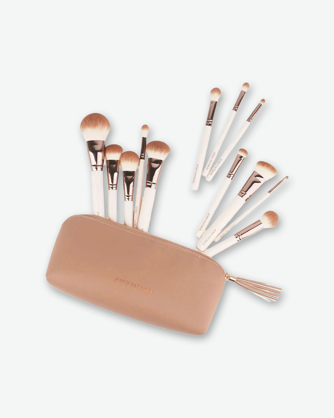 A product shot of a Jenny Patinkin makeup brush set erupting from a tan, faux-leather cosmetic pouch, angled against a plain light gray background. A total of eleven professional makeup brushes—featuring smooth cream-colored handles, rose-gold metal ferrules, and soft brown-and-white bristles—are artistically arranged as if fanning out from the open, zippered pouch.