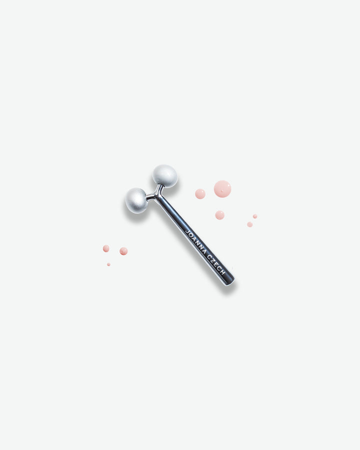 Silver facial roller with pink dots on a white background