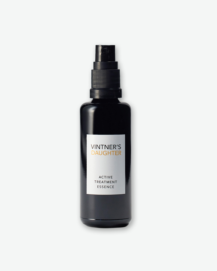 Vintner's Daughter Active Treatment Essence in a dark black glass bottle with a black spray pump nozzle and a vertical white label, isolated against a light grey background.